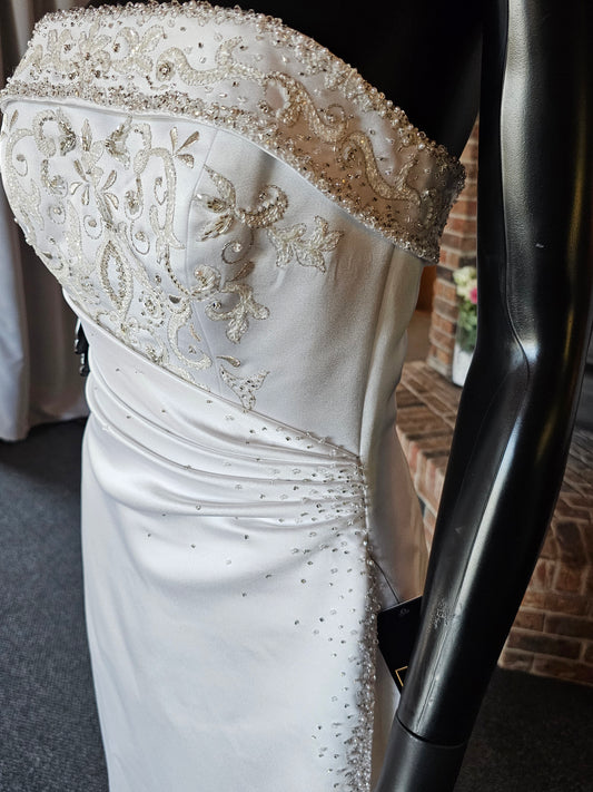 Maggie Sottero Wedding Gown This gorgeous designer gown features a straight, banded neckline with lots of beads and embroidery. The asymmetrical side sweep adds interest and creates a lovely waistline. The creamy white satin is lustrous and falls to a small sweep train. This gown is part of our consignment collection and has been worn before and slightly altered. It is in excellent condition and is ready to be loved again!
