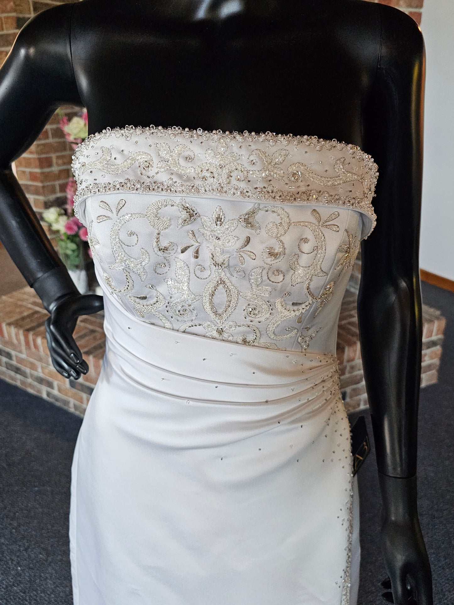 Maggie Sottero Wedding Gown  This gorgeous designer gown features a straight, banded neckline with lots of beads and embroidery. The asymmetrical side sweep adds interest and creates a lovely waistline. The creamy white satin is lustrous and falls to a small sweep train.   This gown is part of our consignment collection and has been worn before and slightly altered. It is in excellent condition and is ready to be loved again! 