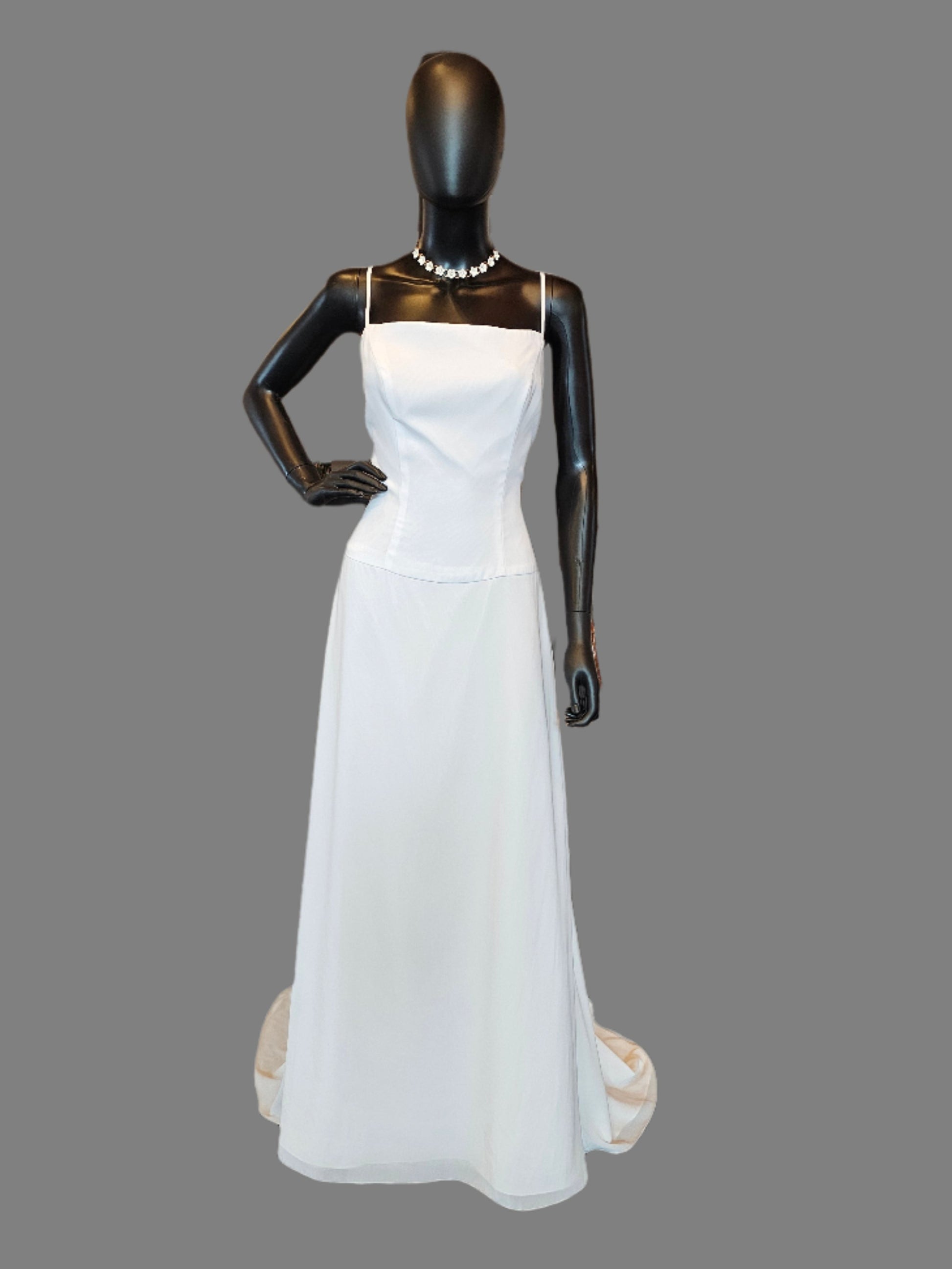 A white chiffon spaghetti strap wedding gown displayed on a mannequin, featuring a scoop neckline, spaghetti straps, a dropped waist, and a sweep train.